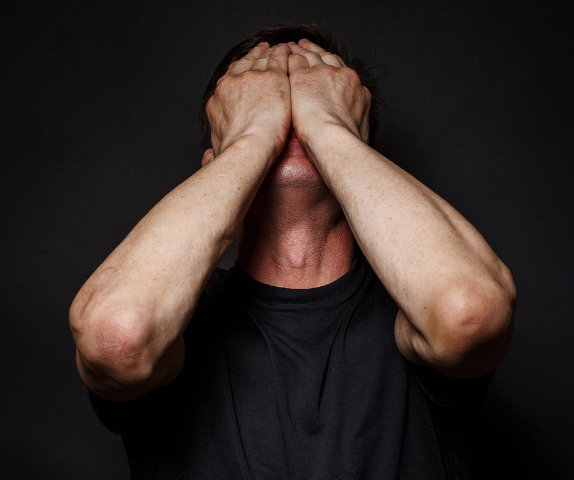 man with head up and palms over face in need of drug addiction therapy